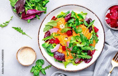 Vegan salad with baked beets, tangerine, red onion, lettuce, sesame and arugula, gray background, top view photo