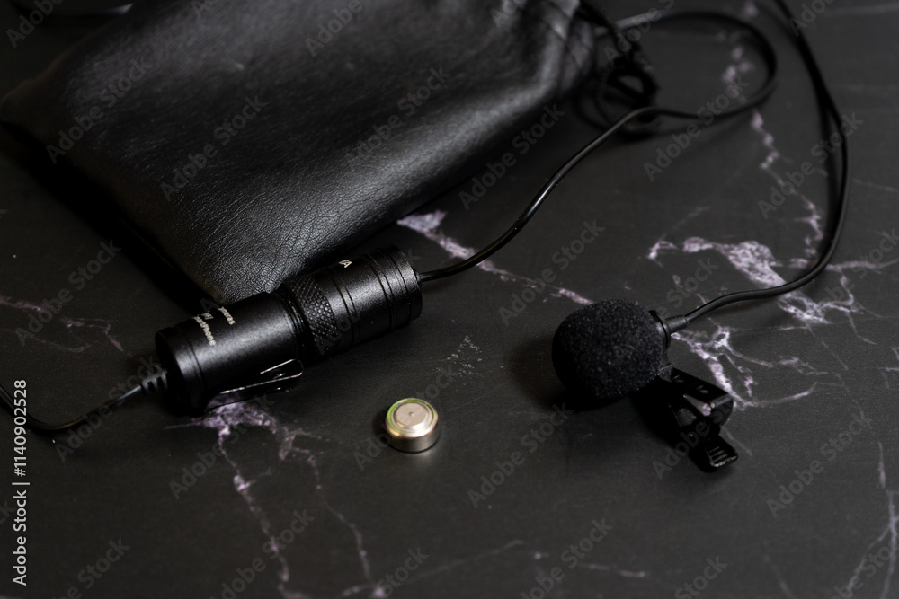 Lavalier microphone on a black background with a spare battery and an eco-leather case. Lavalier microphone on a black background with a spare battery and an eco-leather case.