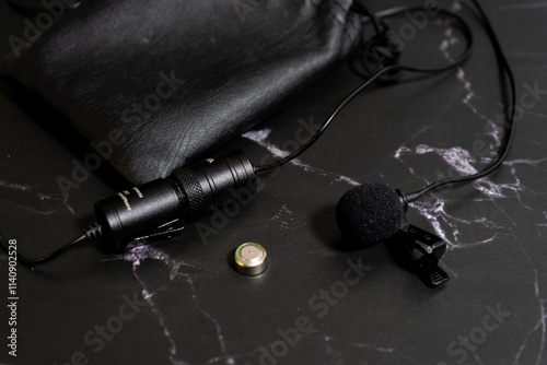 Lavalier microphone on a black background with a spare battery and an eco-leather case.