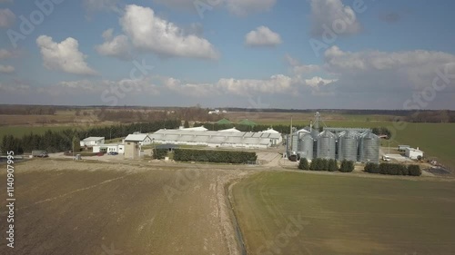 The view from the height of a large farm located among the green hilly fields. Video from a drone or a quadro. Agro-industrial complex with stainless steel silo. Organic food production.Dairy industry