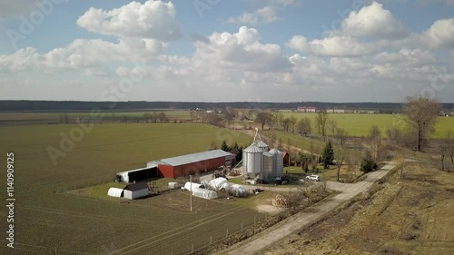 The view from the height of a large farm located among the green hilly fields. Video from a drone or a quadro. Agro-industrial complex with stainless steel silo. Organic food production.Dairy industry