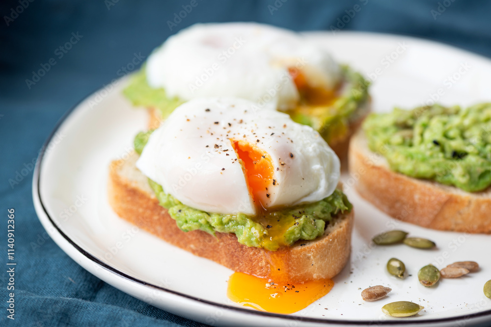 Delicious avocado and poached egg toast with pumpkin seeds on a white plate, closeup view Delicious avocado and poached egg toast with pumpkin seeds on a white plate, closeup view