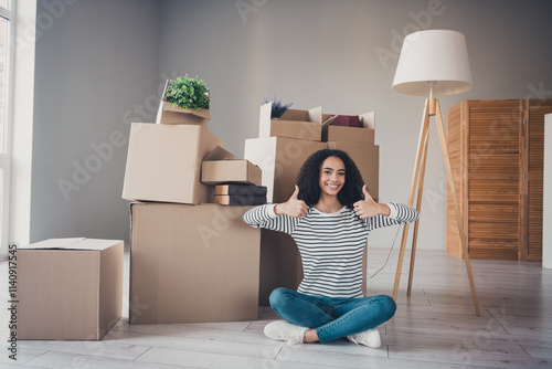 Full size photo of pretty young girl sit floor thumb up pile stack box package living room relocate apartment indoors photo