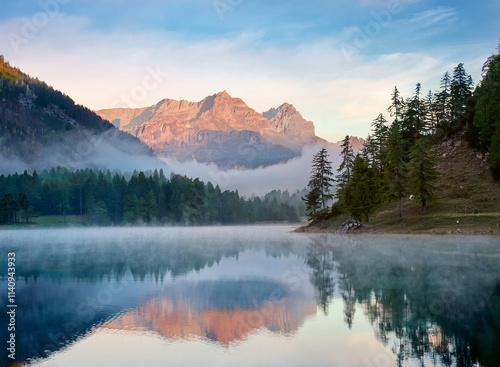A tranquil mountain lake with morning mist and reflections.