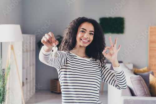 Photo of lovely cheerful girl hold key mortgage ownership show okey dressed striped garment spend pastime spacious house indoors room