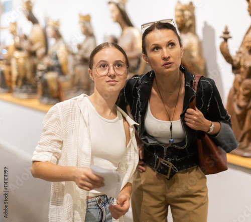 Adult woman and teenage girl with brochure looking at sculptures in museum hall