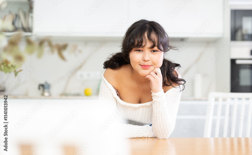 Portrait of smiling young housewife in white blouse and denim skirt standing in kitchen, posing on camera Portrait of smiling young housewife in white blouse and denim skirt standing in kitchen, posing on camera