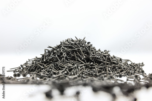 A small pile of black screws on a white background. Fastening materials for fastening drywall structures