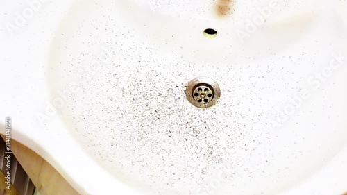 A sink with a drain covered in hair and debris. The sink is white and has a silver drain