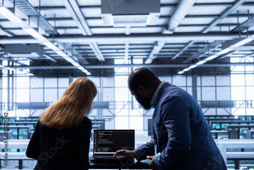 Computer scientists in data center tracking network traffic and activity, installing and configuring software updates. Coworkers performing database backups on notebook to protect user information