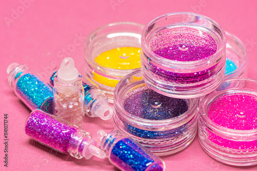 Collection of small plastic containers filled with various colors of glitter, on a pink surface. The vibrant and diverse colors of the glitter. Crafts, makeup, decoration concepts photo