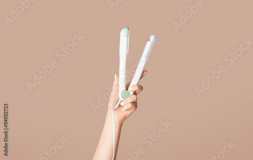 Millennial woman holding hair straightener on pink background, closeup. Panorama