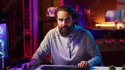 Content creator playing videogames live while chatting with online audience from neon lit apartment. Pro gamer streaming multiplayer game while discussing his strategies with viewers