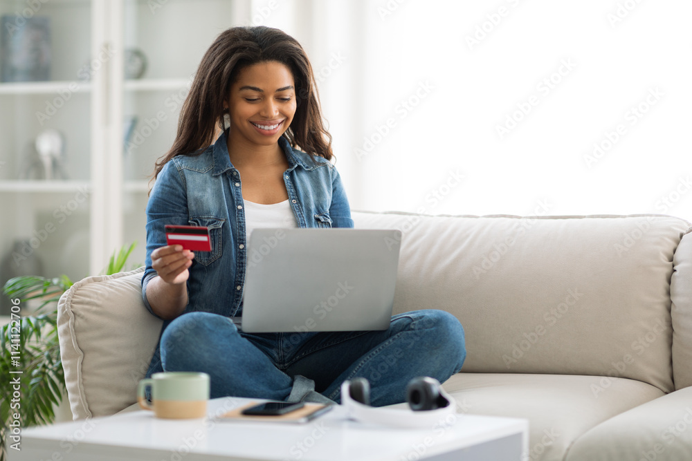 A young woman is happily shopping online on her laptop while relaxed on a cozy sofa. She holds a credit card in her hand, clearly enjoying the experience, copy space A young woman is happily shopping online on her laptop while relaxed on a cozy sofa. She holds a credit card in her hand, clearly enjoying the experience, copy space