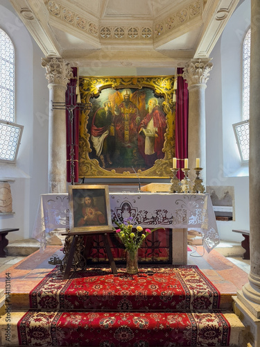 Korcula, Croatia - June 30, 2024: Saint Mark Cathedral. Main altar and chancel with large painting and stone baldaquin. Flowers and Sacred Heart painting in front