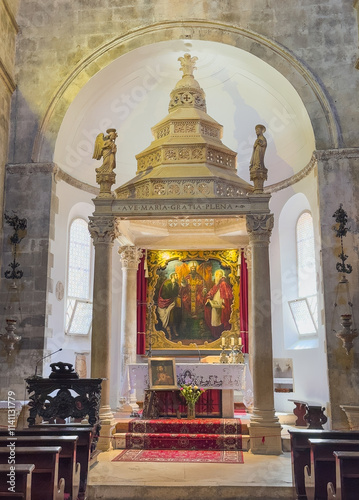 Korcula, Croatia - June 30, 2024: Saint Mark Cathedral. Main altar and chancel with large painting and stone baldaquin and stone angel statues, Dark wooden benches in front