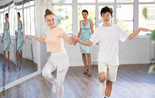 Cheerful enthusiastic teenage girl and boy rehearsing jive dance moves as couple in bright studio under female choreographer watchful eye.. photo