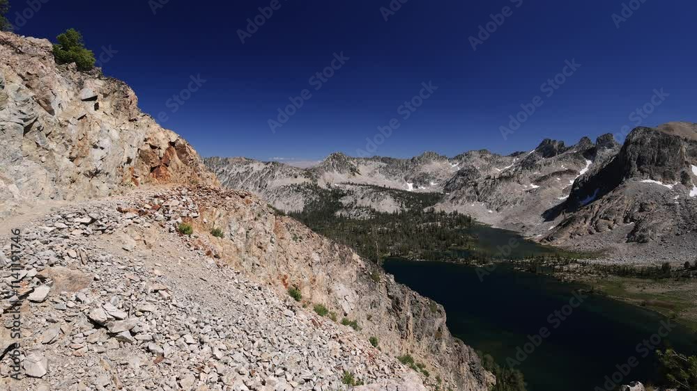 From Snowyside Pass in Idaho's rugged Sawtooth Mountains, two backpackers descend a rocky trail. Below, the Twin Lakes shimmer in the valley below, reflecting the blue sky on a perfect summer day. From Snowyside Pass in Idaho's rugged Sawtooth Mountains, two backpackers descend a rocky trail. Below, the Twin Lakes shimmer in the valley below, reflecting the blue sky on a perfect summer day.