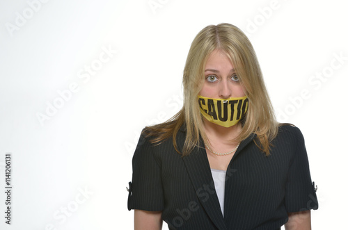 Attractive business woman in suit posing in studio against white background with caution tape across her mouth - eyes wide - illustrating care with protected health information
