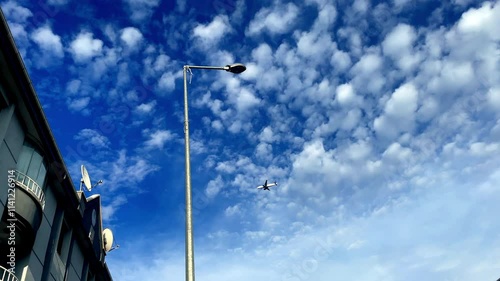 A blue sky with clouds and a plane flying in it. The sky is clear and bright, and the clouds are fluffy and white. The plane is flying low, and it is the only object in the sky. The scene is peaceful