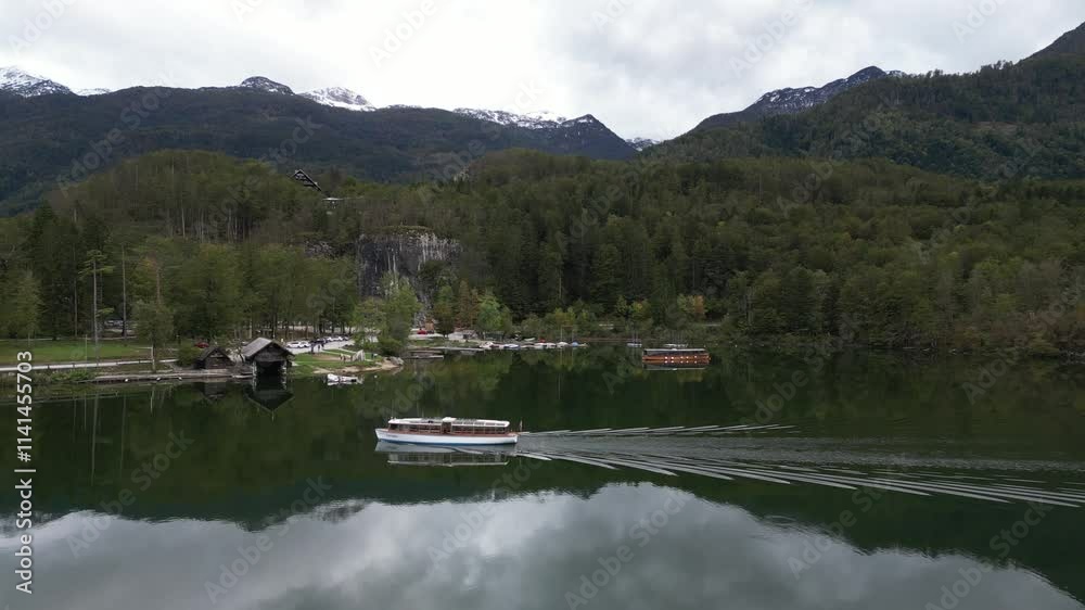 drone shot of boat floating through crystal clear alpine lake with glassy reflection in Triglav National Park in Slovenia drone shot of boat floating through crystal clear alpine lake with glassy reflection in Triglav National Park in Slovenia