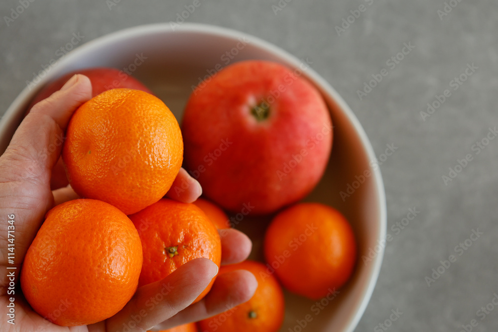 In a bowl, there are tangerines and apples. A hand is holding tangerines. In a bowl, there are tangerines and apples. A hand is holding tangerines.