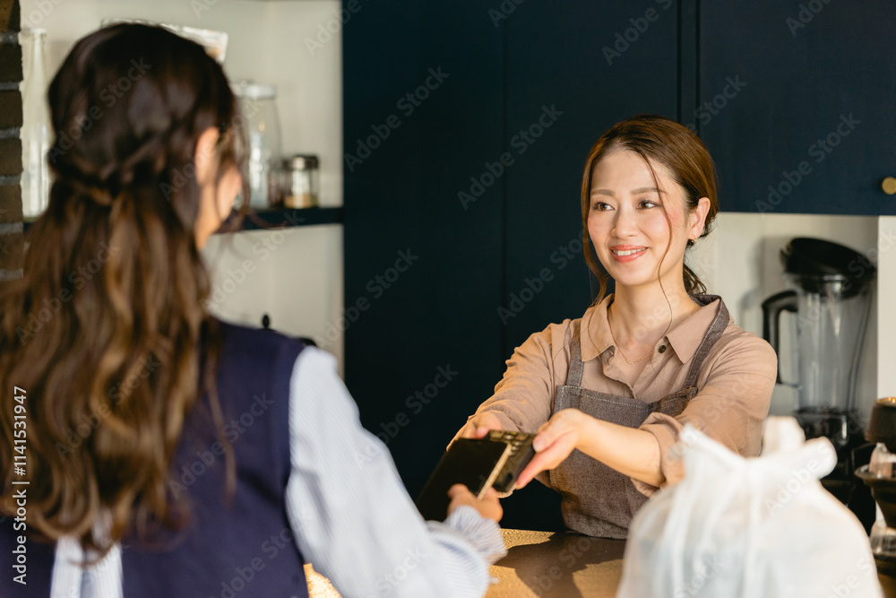 Obraz premium カフェでスマホ決済をする女性（飲食店・テイクアウト）