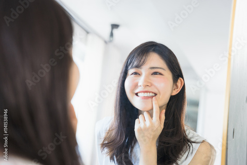 姿鏡の前で鏡に映る自分の歯の調子を眺めて笑顔になる20代?30代の女性 photo