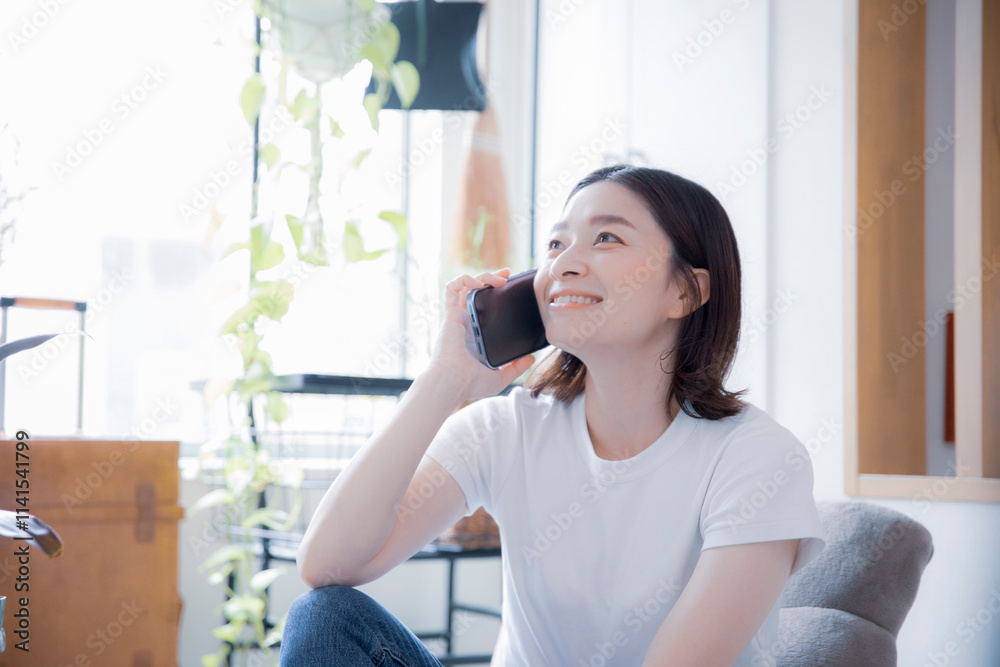 明るい室内でスマートフォンで笑顔で通話する日本人女性