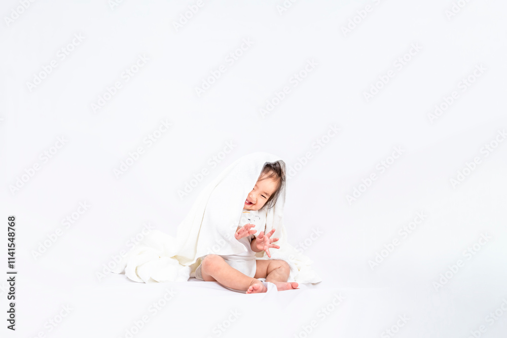 Obraz premium 白背景の前に座りバスタオルを被り笑う1人の女の子の赤ちゃん