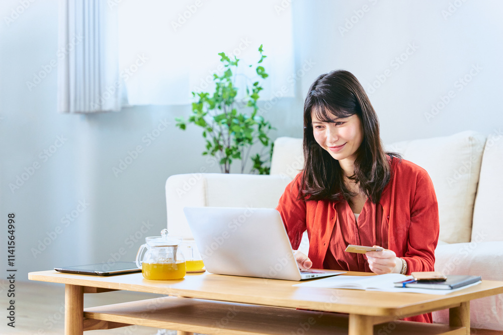 明るいリビングでクレジットカードを手に持ちインターネットショッピングをする為に検索をする30代の女性 明るいリビングでクレジットカードを手に持ちインターネットショッピングをする為に検索をする30代の女性