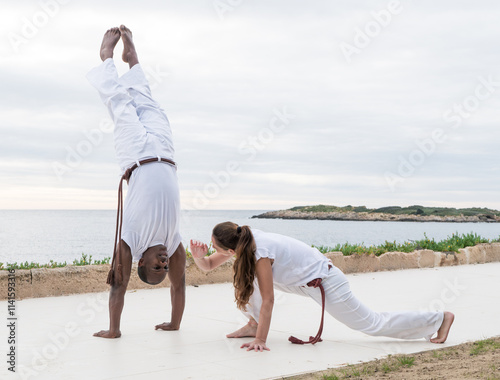 Two people practicing capoeira on a scenic outdoor terrace near the ocean