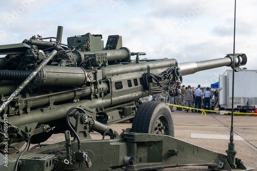 Close-up of a military field artillery cannon on display at an outdoor event, with people in uniform in the background.