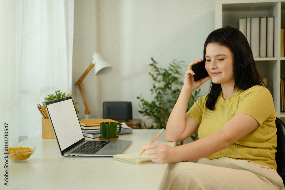 Charming young woman talking on mobile phone and taking notes in a notebook at home Charming young woman talking on mobile phone and taking notes in a notebook at home