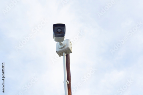 Surveillance camera mounted on pole against cloudy sky, capturing urban life. camera is positioned to monitor area, showcasing modern security technology photo