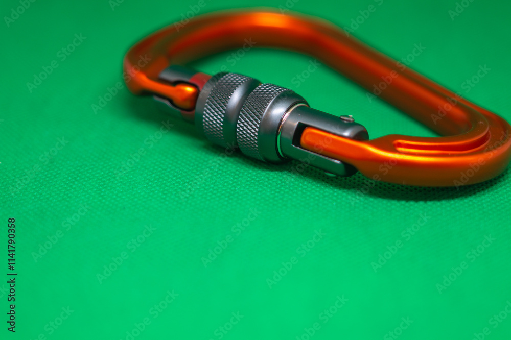Climbing orange carabiner on a green background close-up, selective focus Climbing orange carabiner on a green background close-up, selective focus