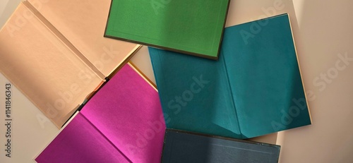 Opened books with colored endpapers lie on the table. Lit by the sun