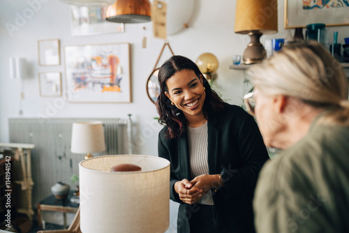 Smiling female owner with senior customer buying electric lamp at antique store photo