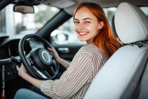 Smiling young female driver in striped blouse driving car with white interior while looking away photo