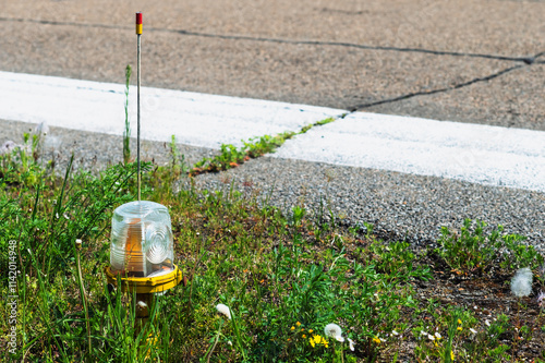 Signal light close up on the edge of the airport runway in summer. Selective focus. Grass and crack in the asphalt photo