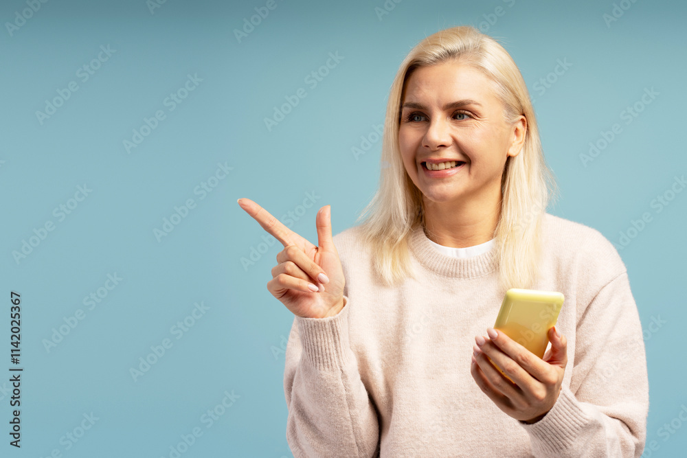 Smiling woman pointing finger and holding smartphone on blue background Smiling woman pointing finger and holding smartphone on blue background