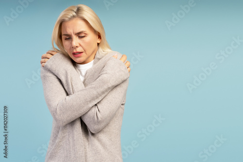 Freezing mature woman hugging herself on blue background