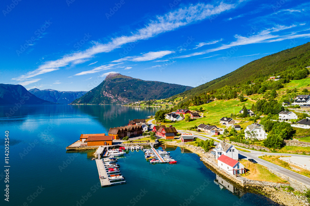 Obraz premium Majestic view of Norwegian fjord with serene waters and charming village under bright blue sky