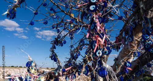 A tree adorned with vibrant Nazar amulets, also known as the Evil Eye, stands under the clear blue sky, symbolizing protection and tradition in Turkish culture.