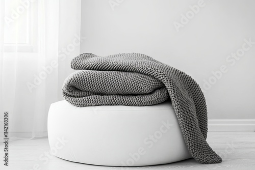 Cozy gray knitted blanket on white ottoman in minimalist living room interior