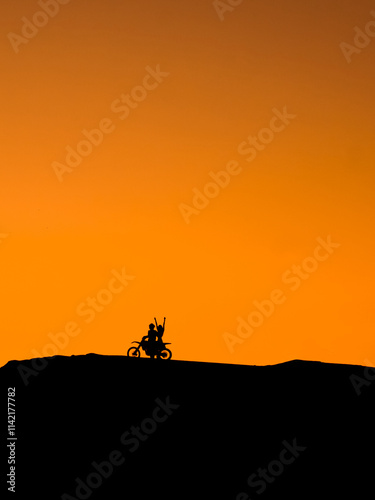 Silhouette of a girl and a man on a motorcycle. Silhouette of a couple and a motorcycle at sunset. Silhouette of a motorcycle racer and a girl at sunset.