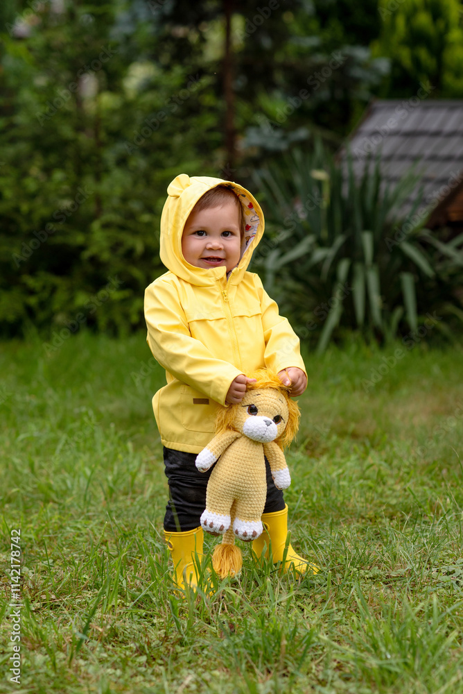 A small child in a yellow raincoat and yellow rubber boots walks through a green meadow. A small child in a yellow raincoat and yellow rubber boots walks through a green meadow.