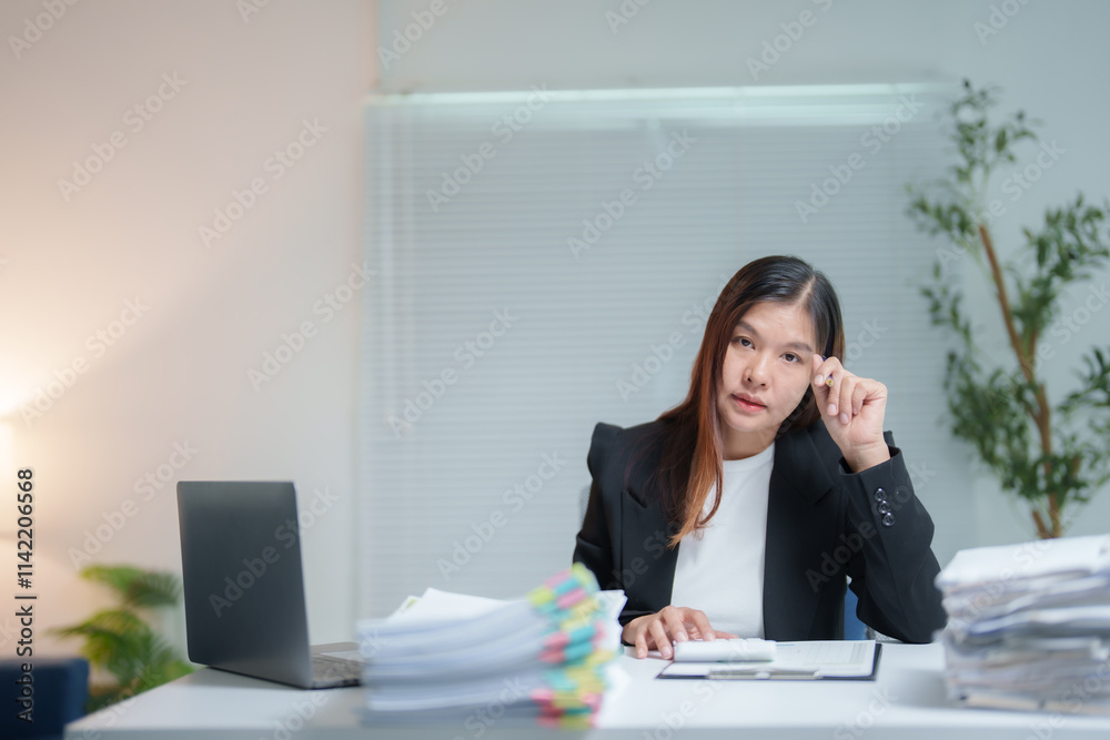 Asian businesswoman sitting at desk and working with laptop and documents, thinking about her job and touching her forehead in modern office Asian businesswoman sitting at desk and working with laptop and documents, thinking about her job and touching her forehead in modern office