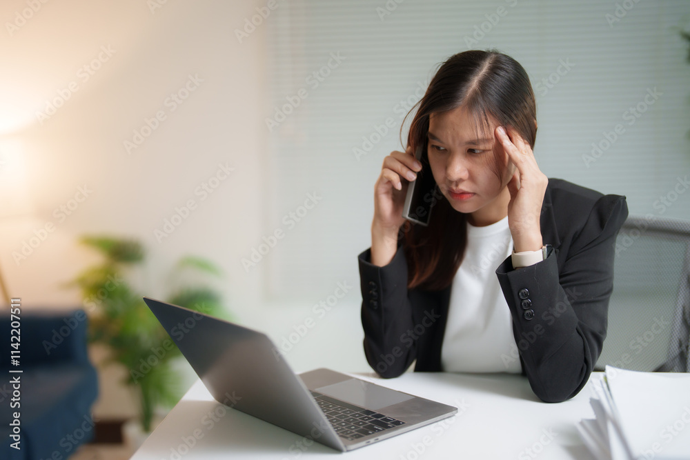 Young professional having a headache while working on a laptop and talking on the phone, experiencing stress and frustration in a modern office environment Young professional having a headache while working on a laptop and talking on the phone, experiencing stress and frustration in a modern office environment