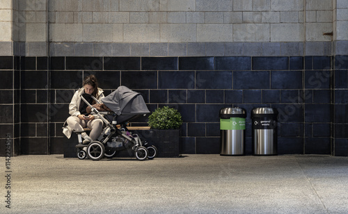 Obraz na płótnie Portrait of Woman using her smartphone while sitting on the bench next to beby in stroller(baby carriage), plant pot and Stainless steel trash cans and recycle bins at resting area inside the shopping w salonie